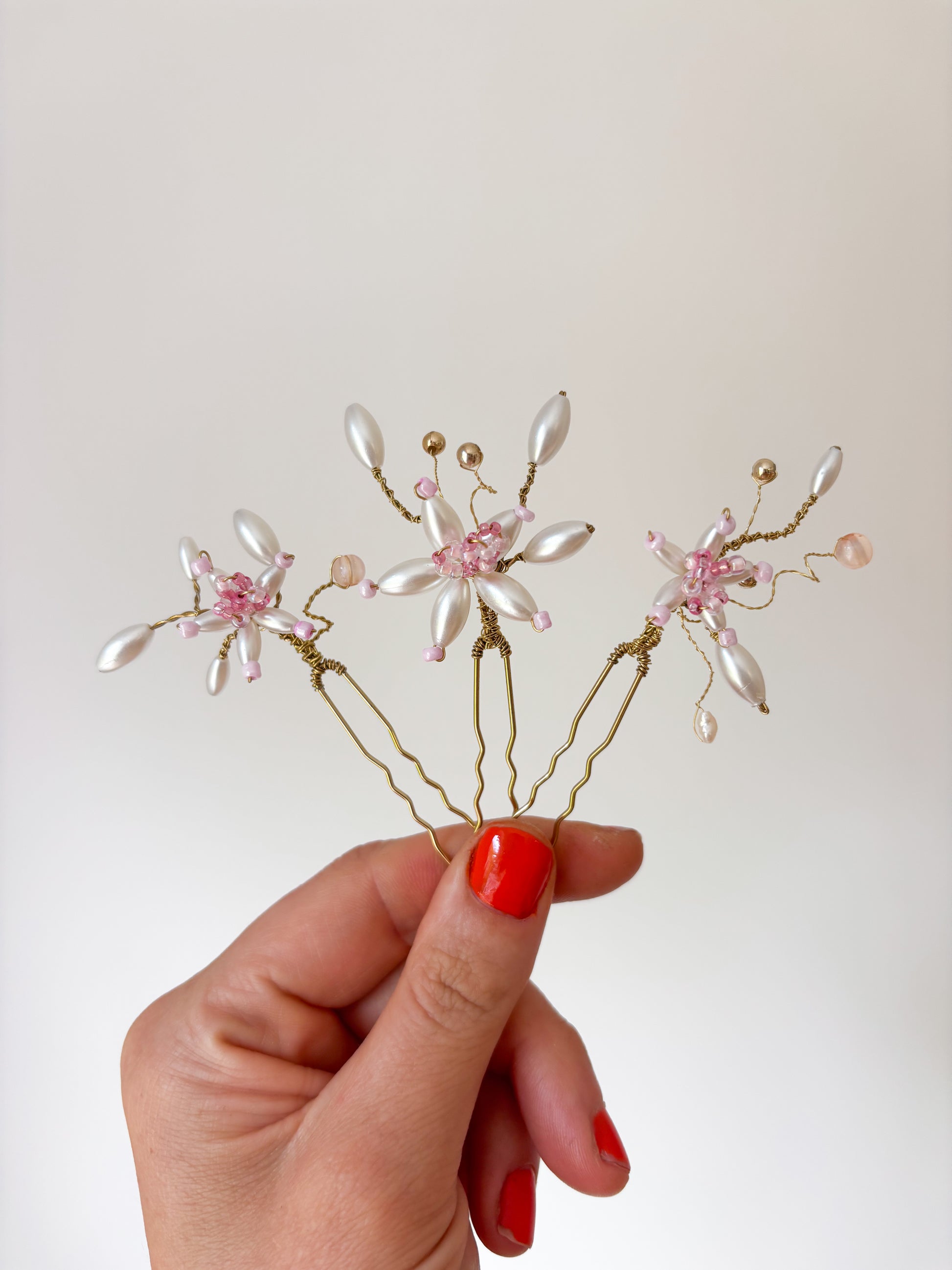 Hand holding a decorative hairpin with floral and pearl details against a plain background